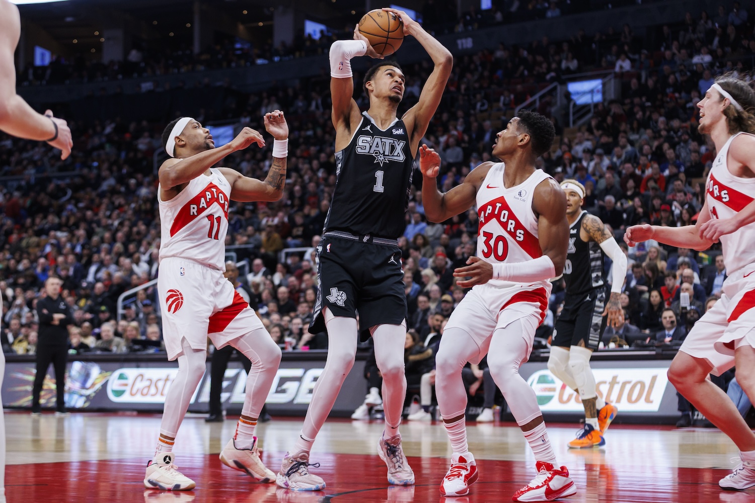 Victor Wembanyama (Wemby) of the San Antonio Spurs looks to the basket as he's defended by Bruce Brown #11 and Ochai Agbaji #30 of the Toronto Raptors in an NBA game on February 12, 2024