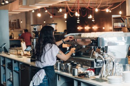 barista with long hair and apron making coffee behind the counter