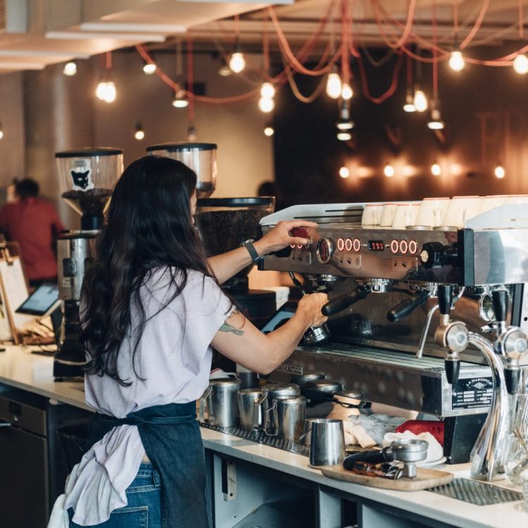 barista with long hair and apron making coffee behind the counter