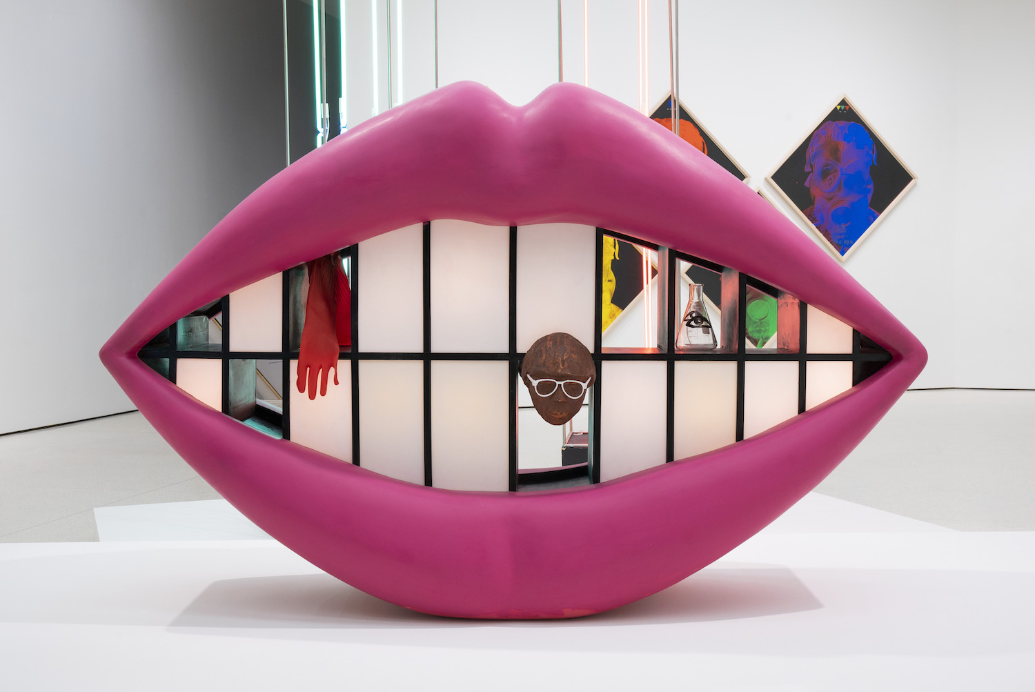 Small statue of a pair of pink lips smiling with teeth and other art pieces inside of the mouth