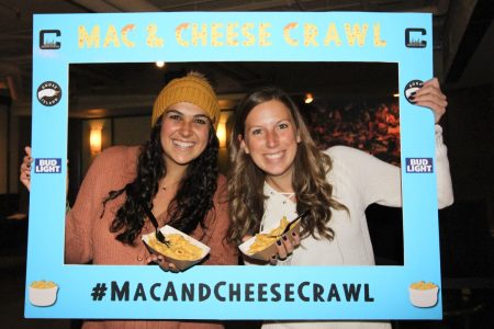 two women holding mac and cheese and #macandcheesecrawl sign
