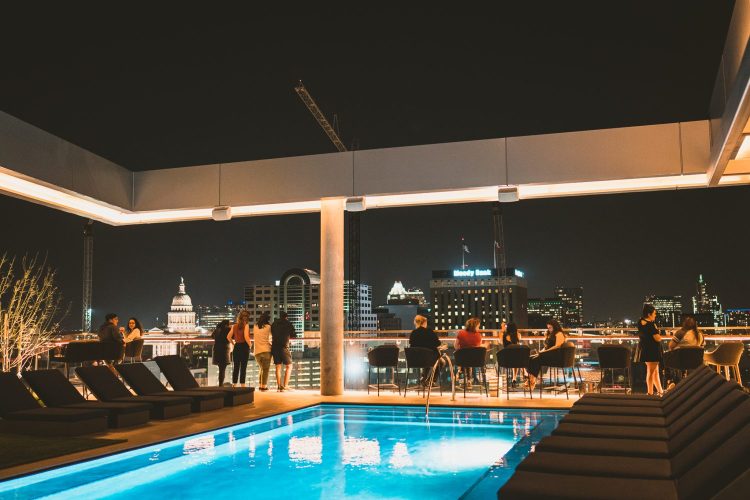pool on a rooftop at night with people looking over the ledge at skyline