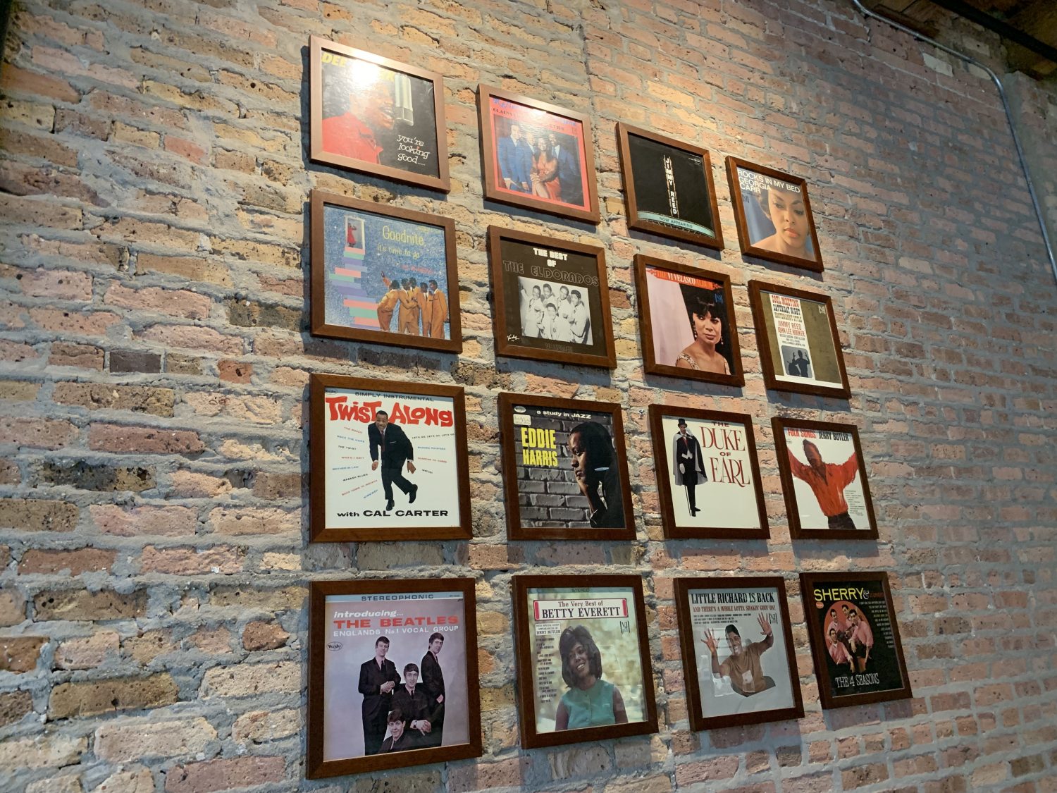 16 framed pictures of albums on a brick wall