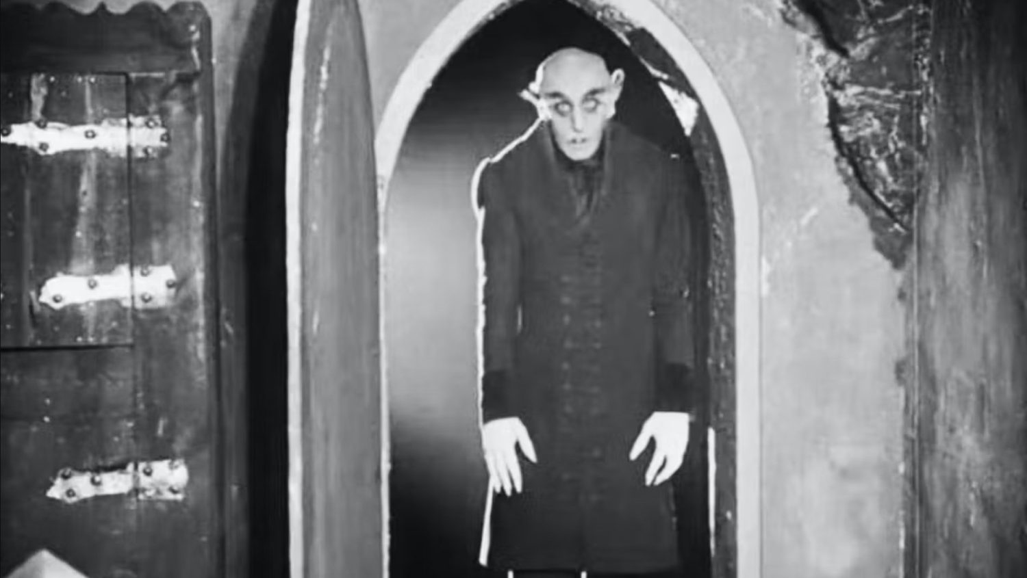 tall vampire in black trench coat standing in doorway