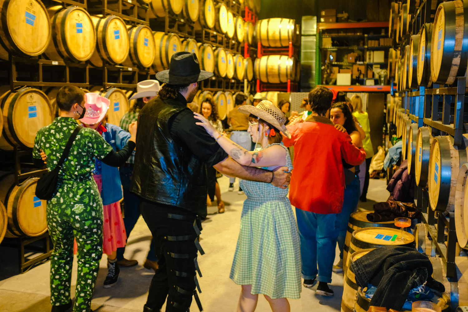 People dancing in country outfits in a room filled with barrels 
