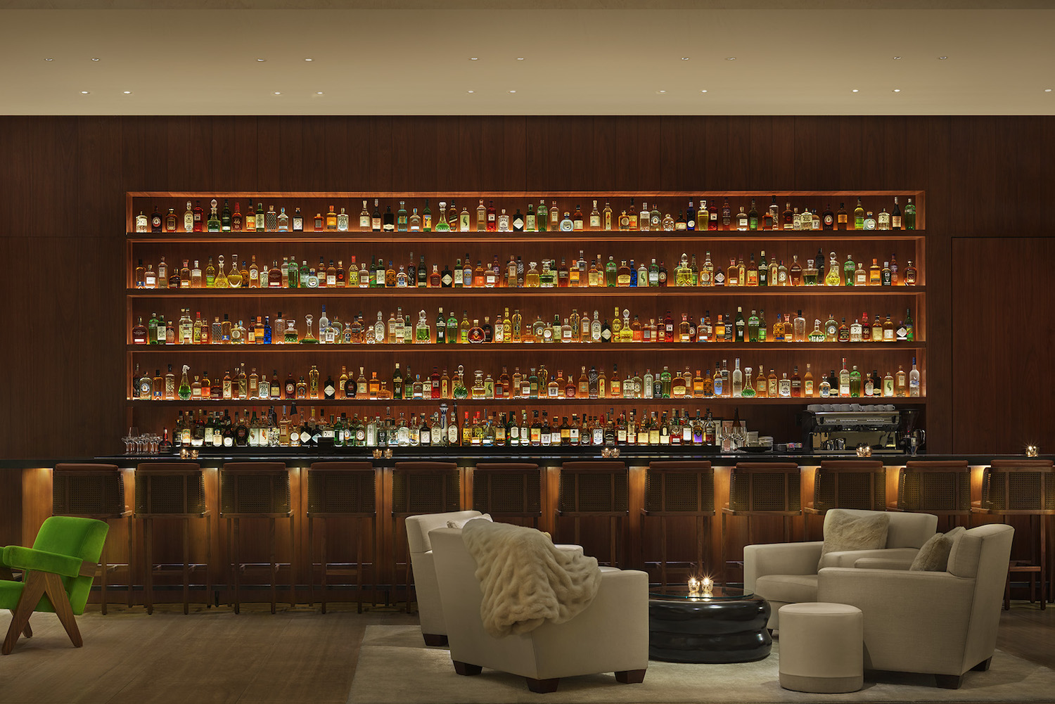 A large dark bar area with an incredibly wide bar rack with dim lighting and a seating area in front of the bar