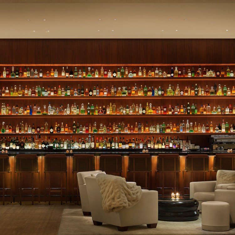 A large dark bar area with an incredibly wide bar rack with dim lighting and a seating area in front of the bar
