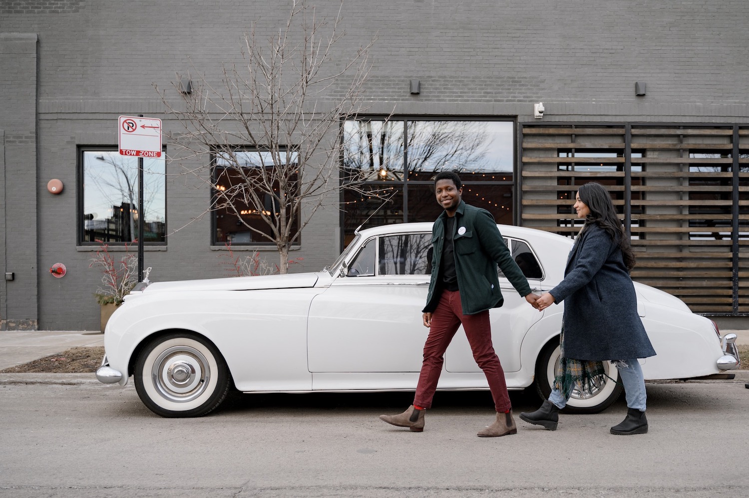 Two people holding hands and walking in front of a white car