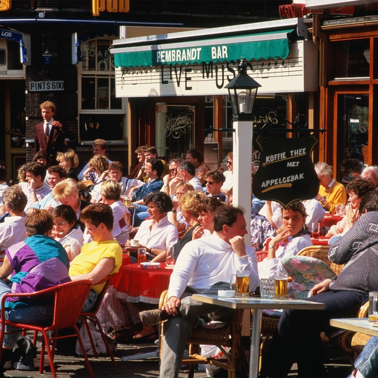 Dozens of people sitting close together at a cafe. Next time you're out and about, keep your headphones in your pocket and practice eavesdropping. It's good for you.