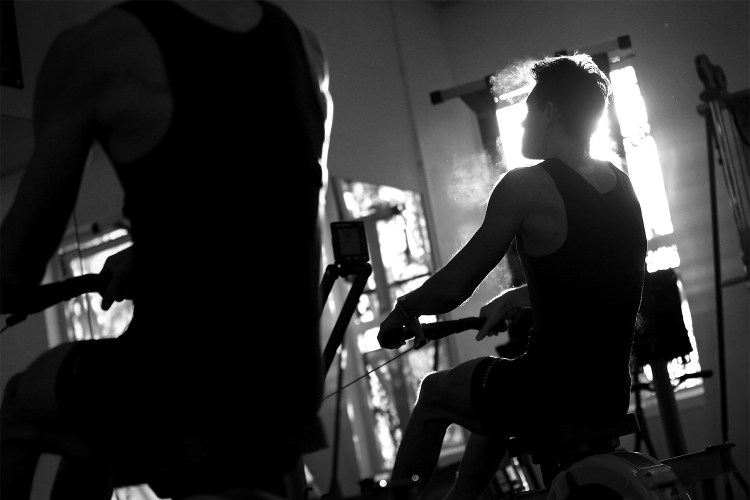 A black and white image of a man breathing out while rowing on an erg. Here's why indoor rowing is such a great cross-training exercise.