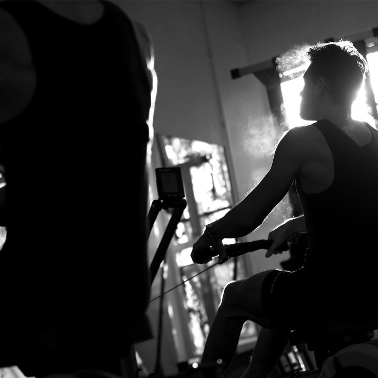 A black and white image of a man breathing out while rowing on an erg. Here's why indoor rowing is such a great cross-training exercise.