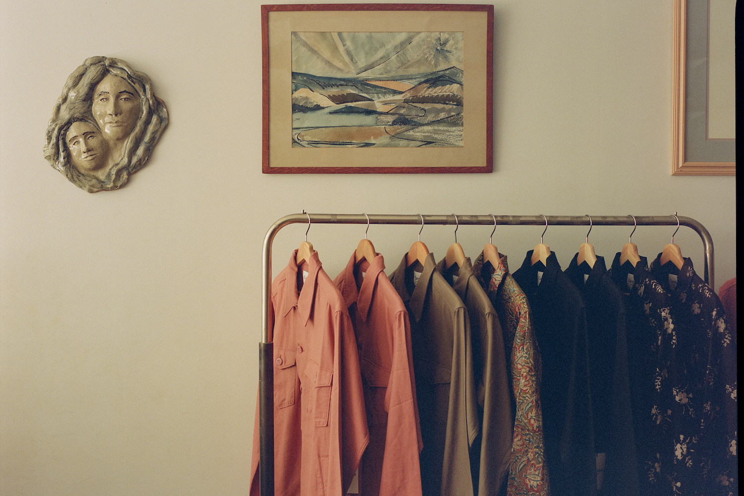 multicolored garments hanging on a rack, painting of mountains on wall, sculpture of faces on wall