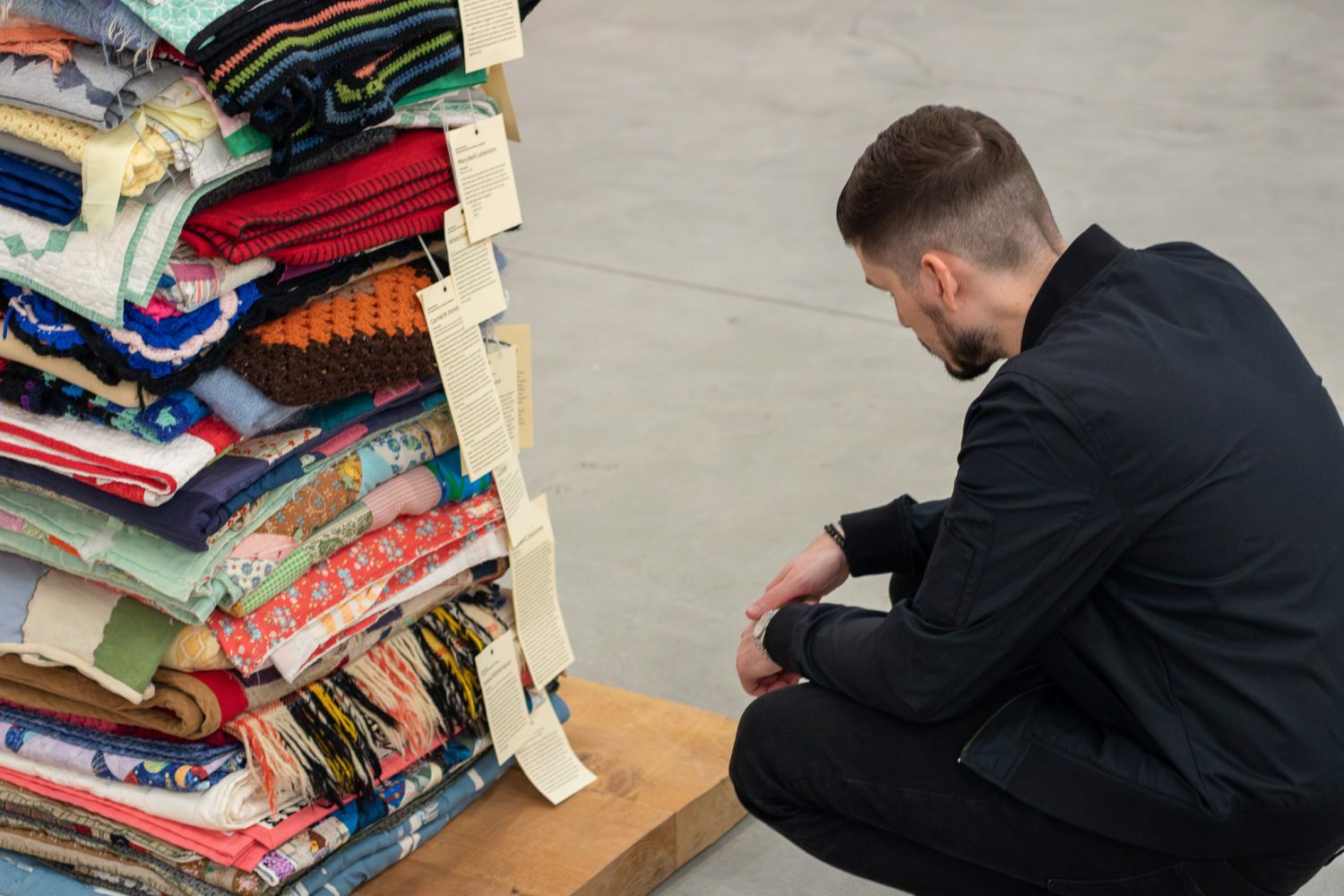 man in black clothes crouching next to art piece of clothes