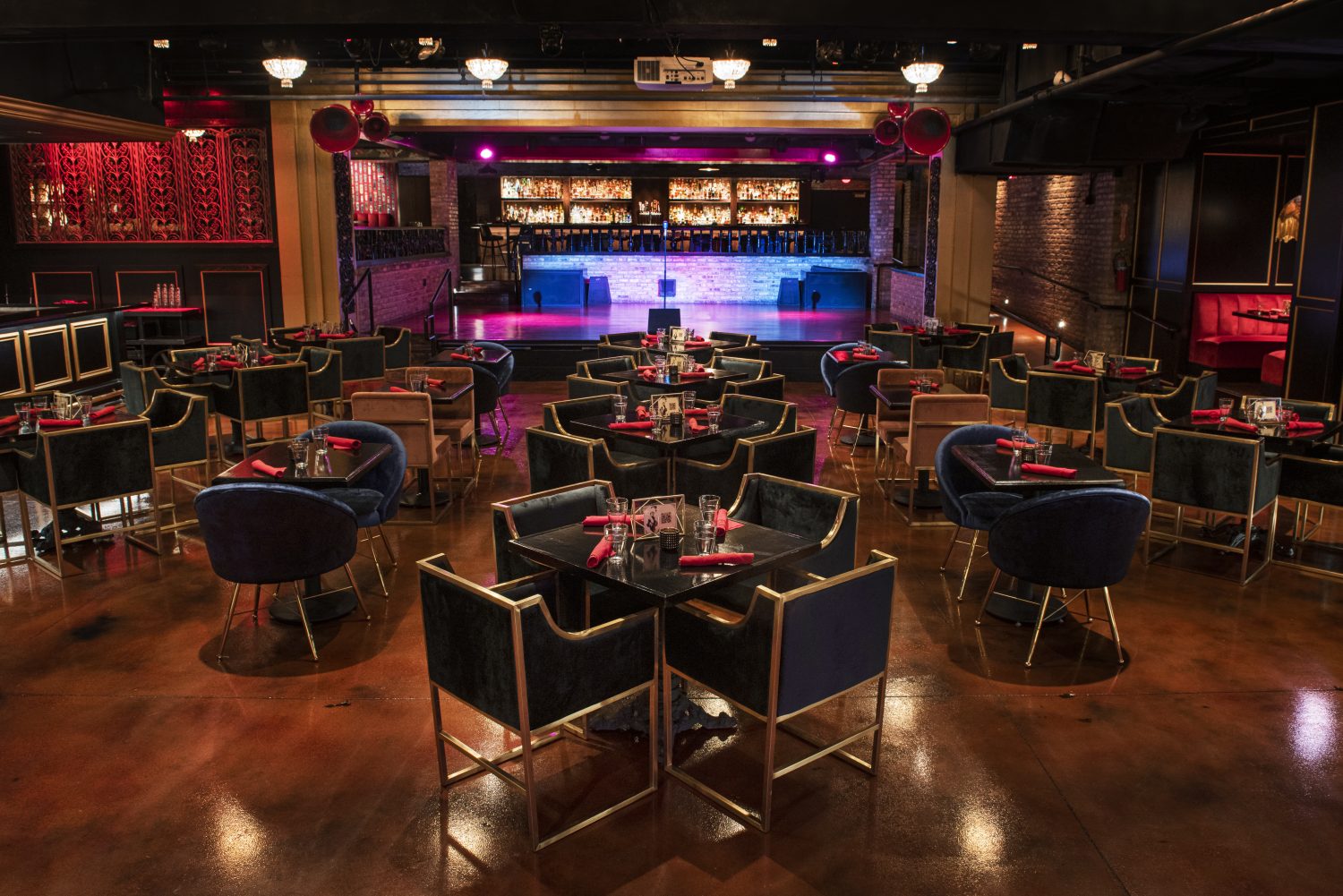 stage with neon lights, tables with blue chairs with gold lining, red napkins