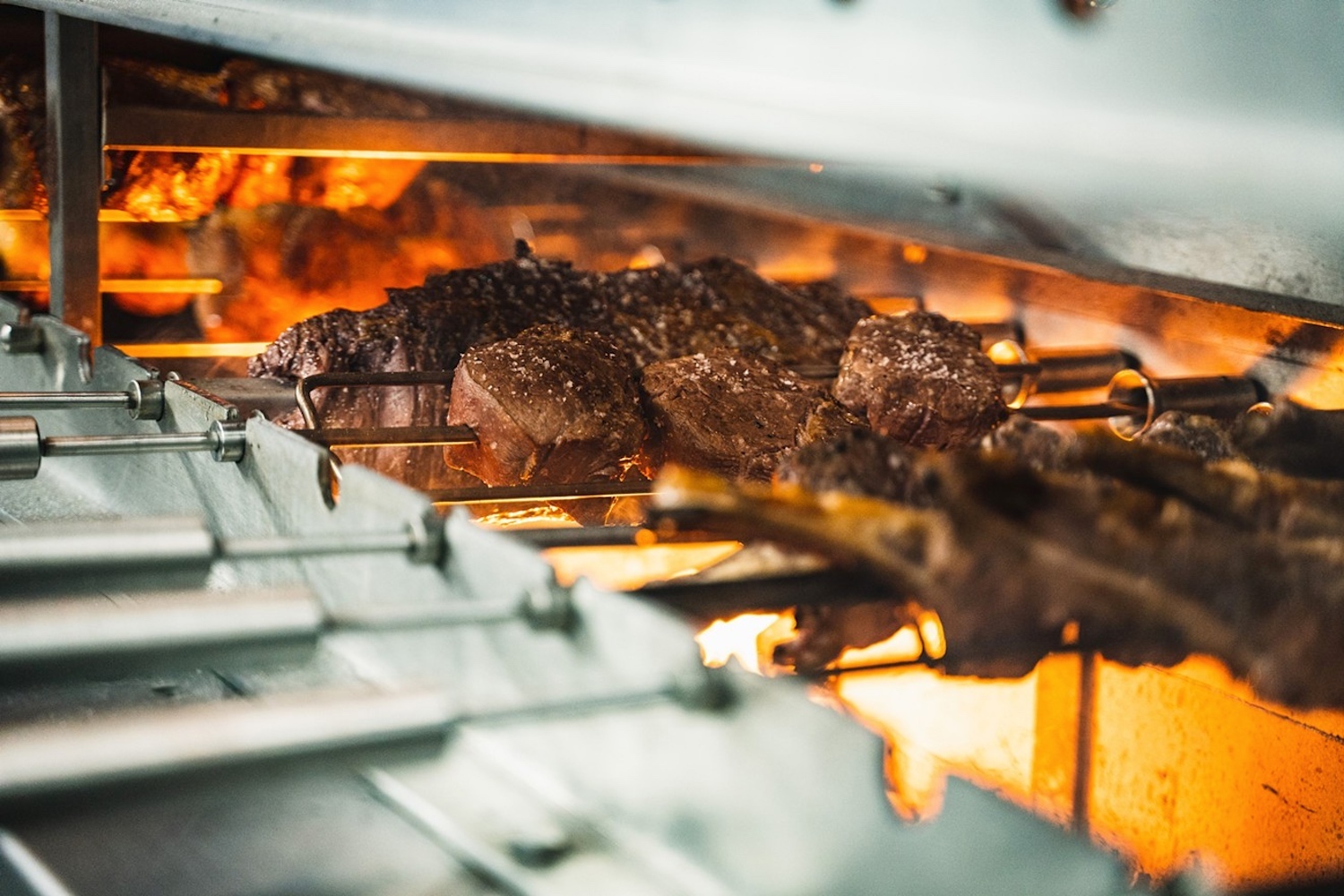 a grill with steak turning on multiple rotisserie skewers