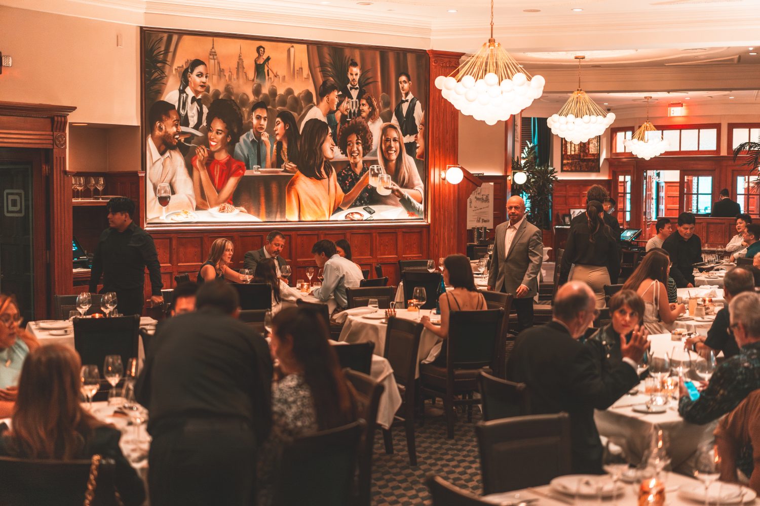 people having dinner, chandeliers, painting on a wall
