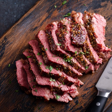 Corned beef cooked and sliced on a cutting board next to a knife