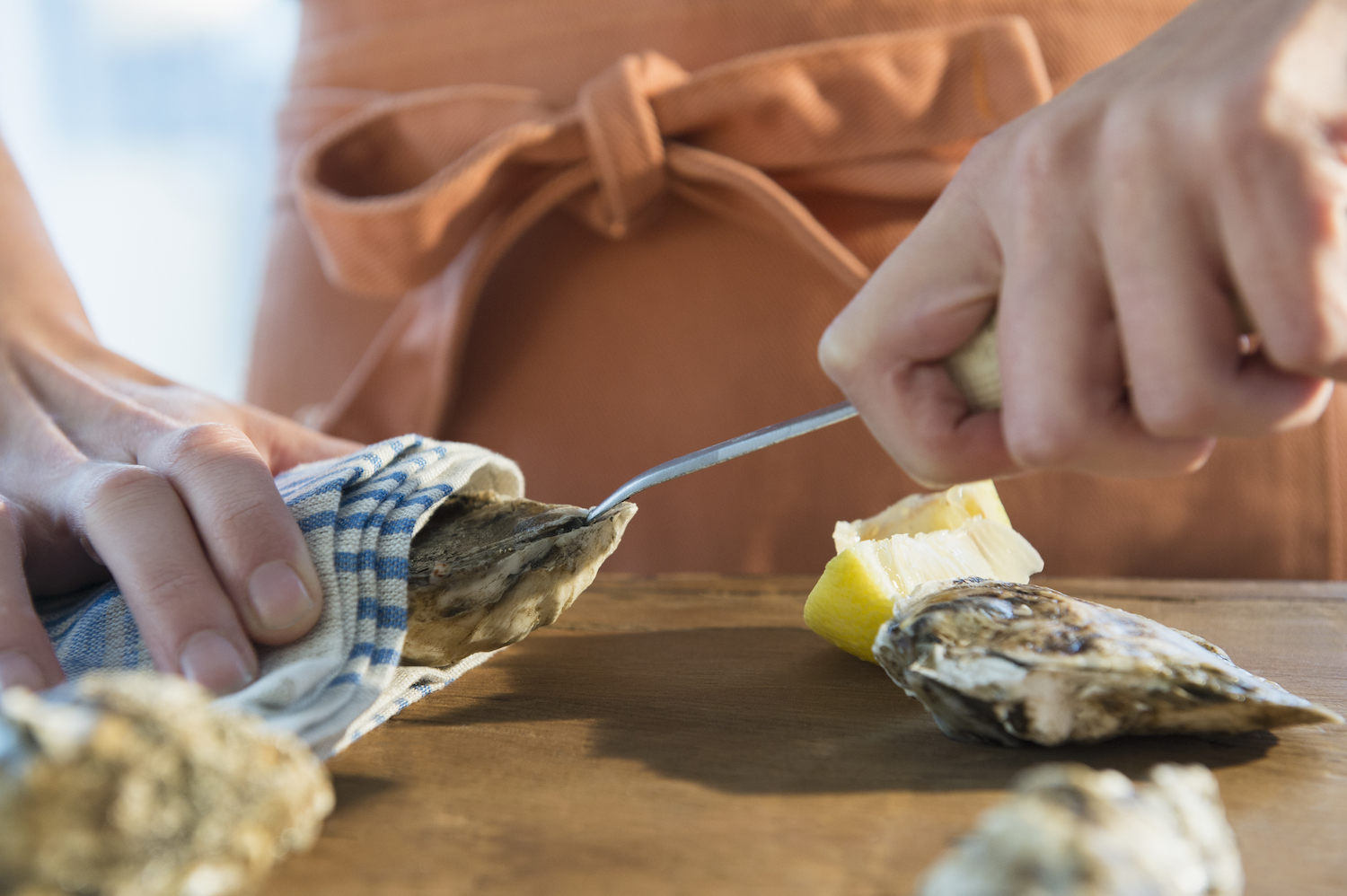 Woman in an orange apron shucking oysters