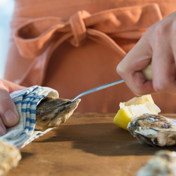 Woman in an orange apron shucking oysters