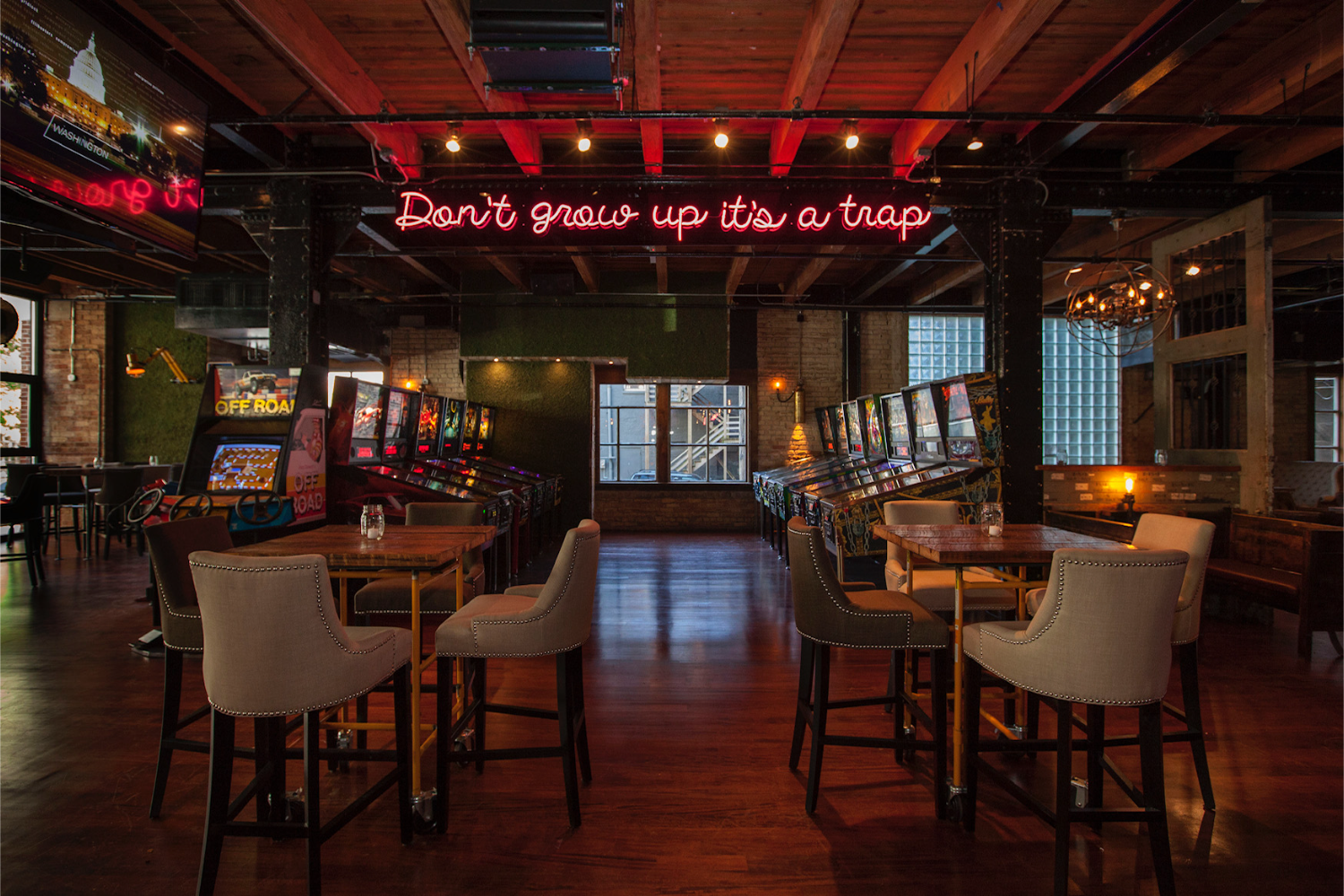 arcade games, tables with chairs, neon red sign that reads "don't grow up, it's a trap"
