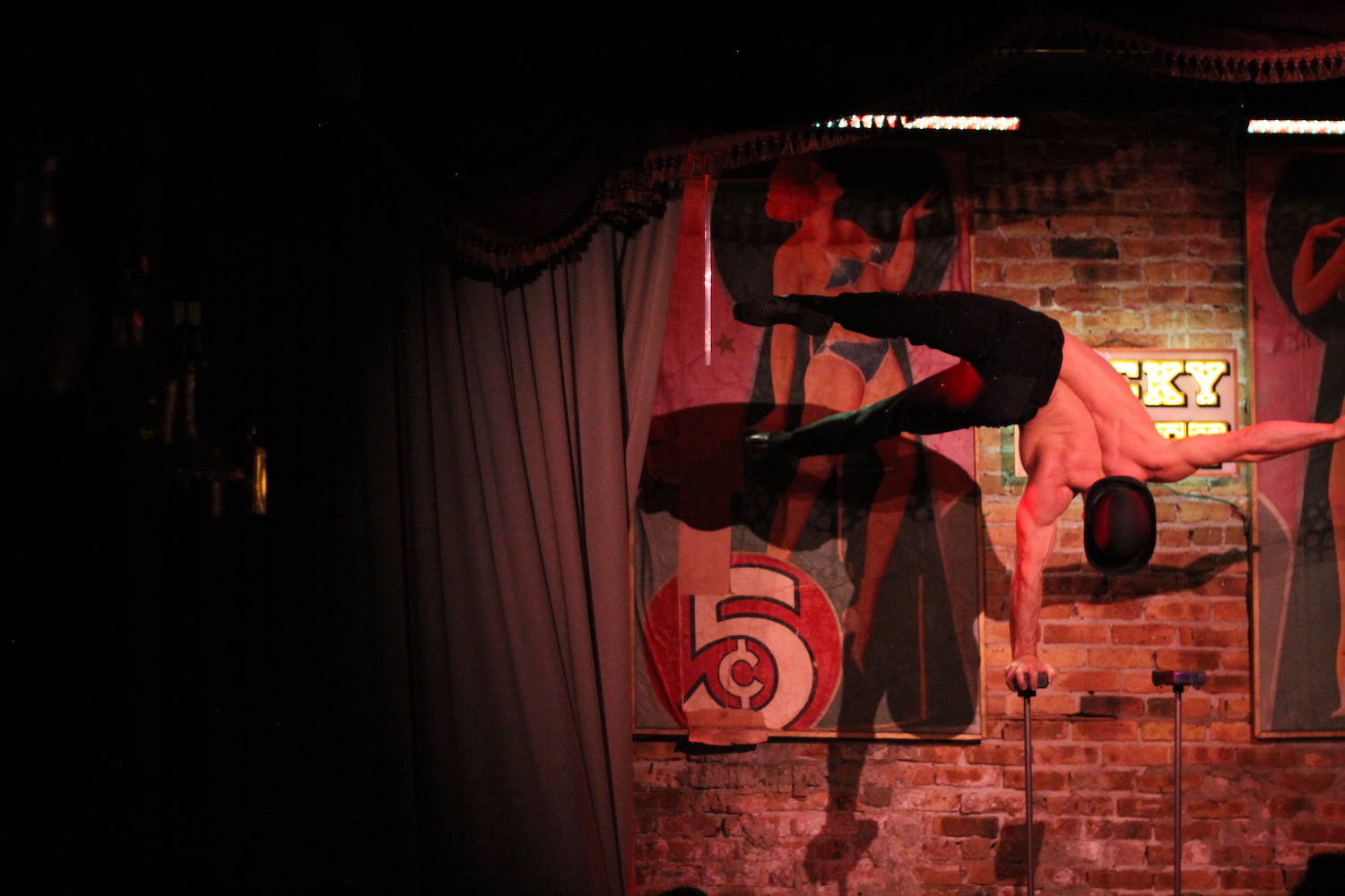 a man holding himself up on a single pole during a burlesque show