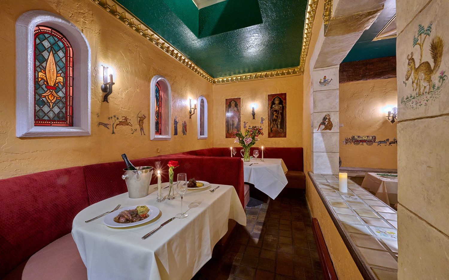 red booths, yellow walls with paintings and loghts hanging, table with tablecloths, food, flowers, and candles
