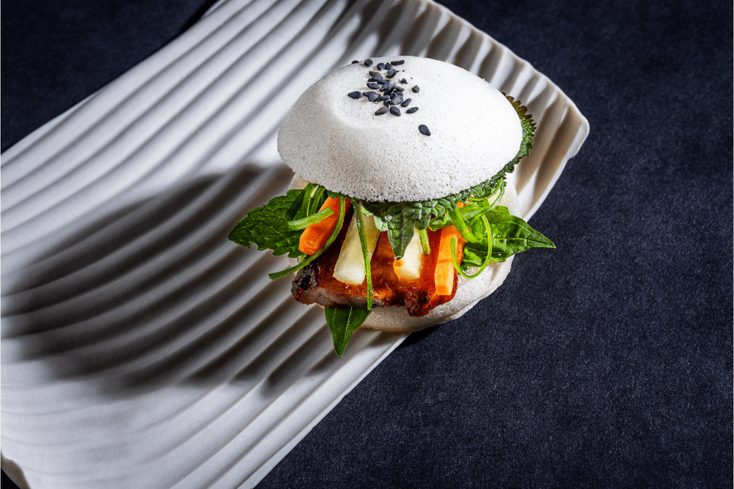 meat and lettuce between two white buns with sesame seeds on a white plate