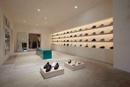 lit up shelves with different colored sneakers on them, white tables with sneakers on top, center teal block, mirror, art on wall
