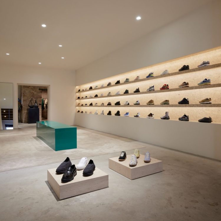 lit up shelves with different colored sneakers on them, white tables with sneakers on top, center teal block, mirror, art on wall