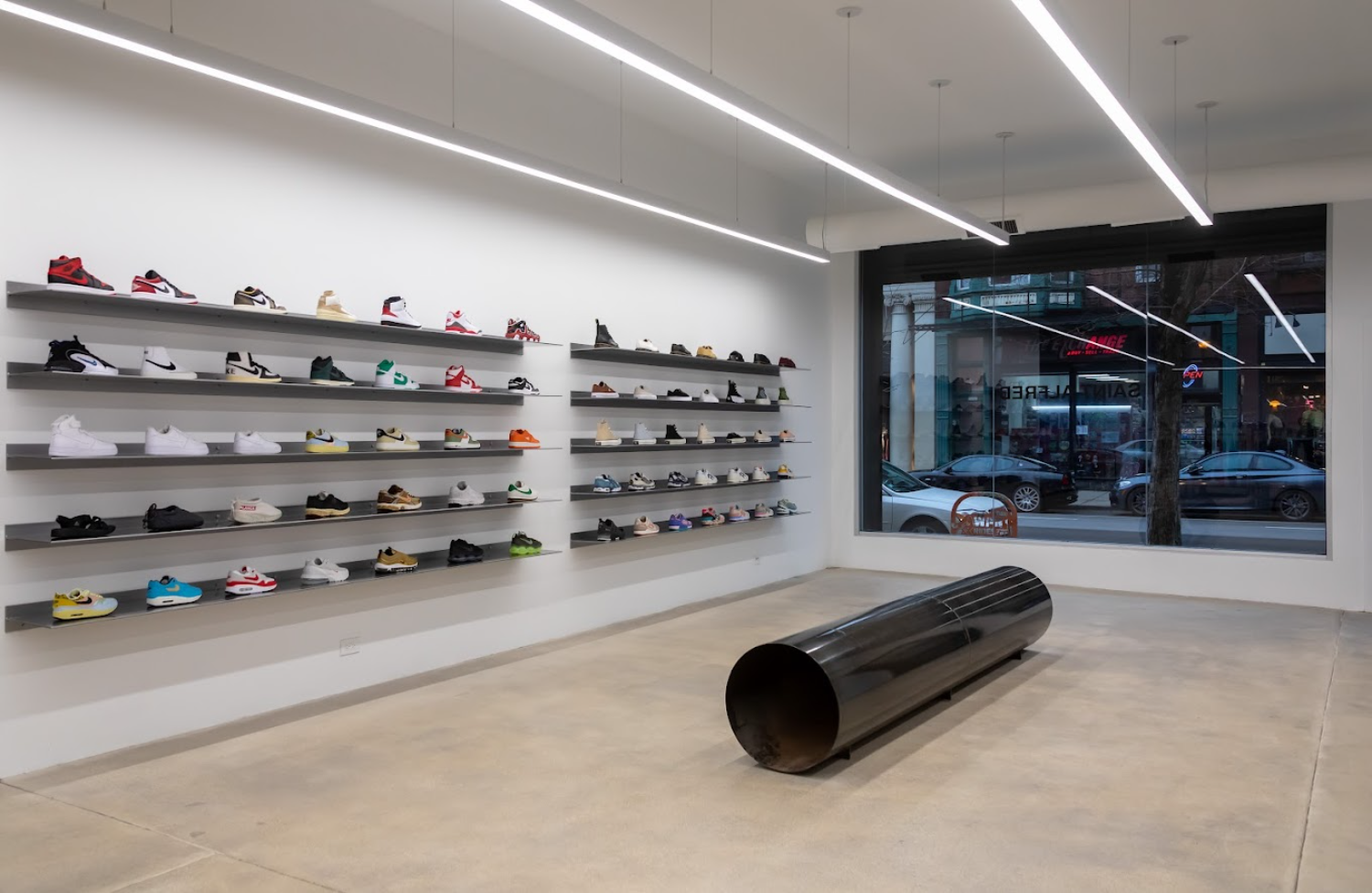 sneakers placed on black shelves, black cylinder on the floor, window facing outdoor street