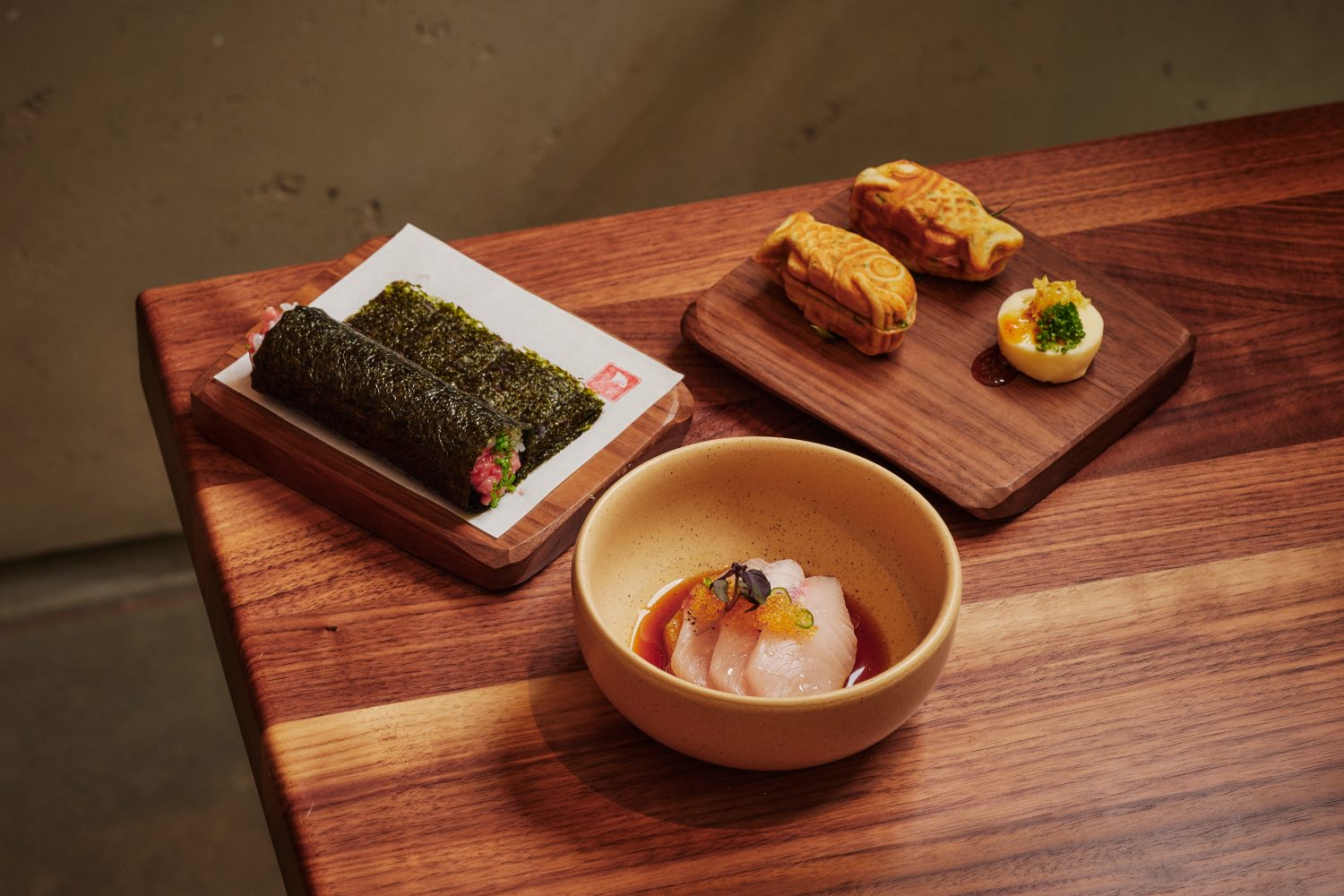 two hand rolls on a plate, three slices of sashimi in a bowl, two fish-shaped pastries 