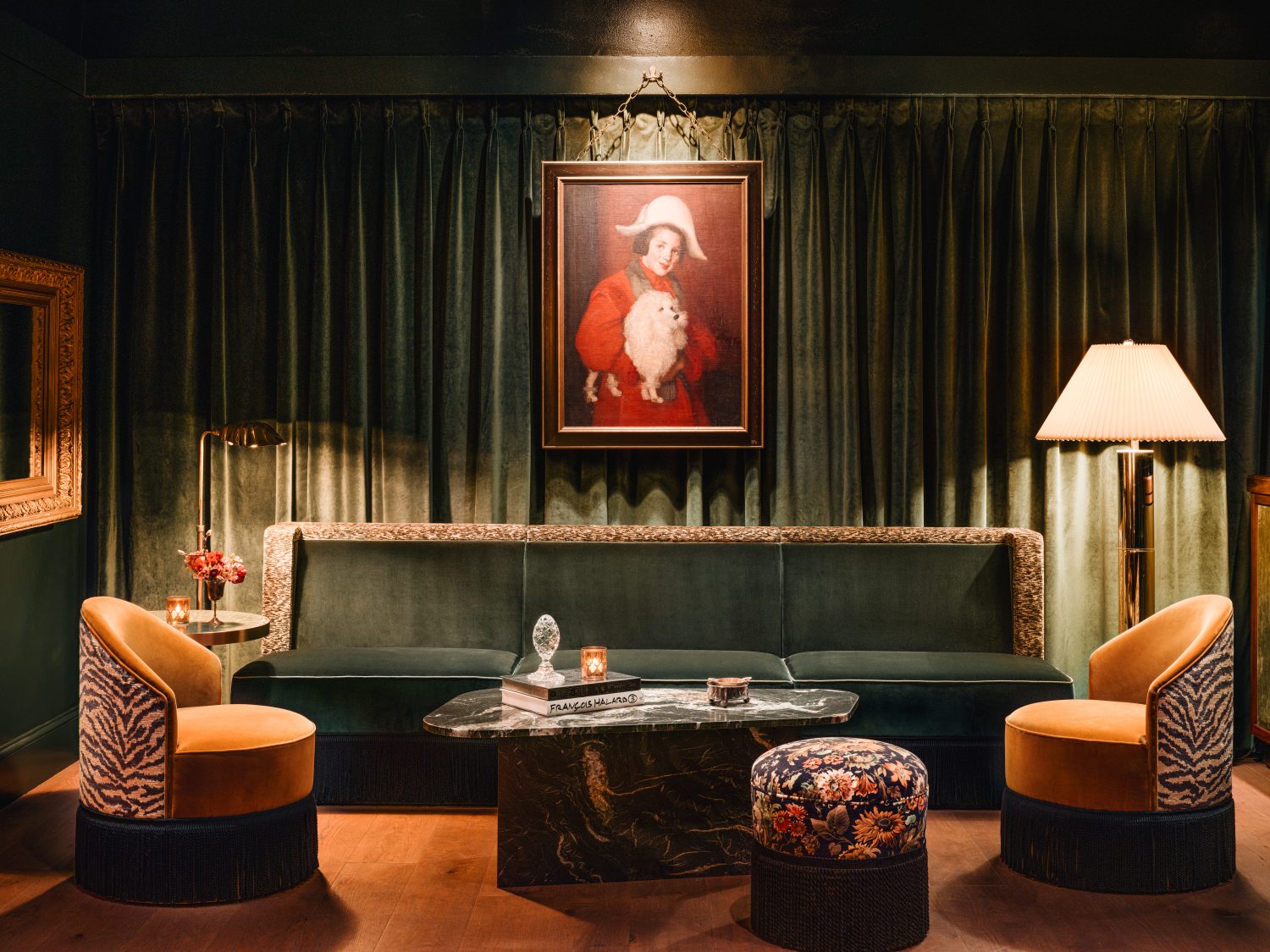 painting of a girl holding a white dog, green couch, green curtains, two chairs, books on a coffee table, lamps