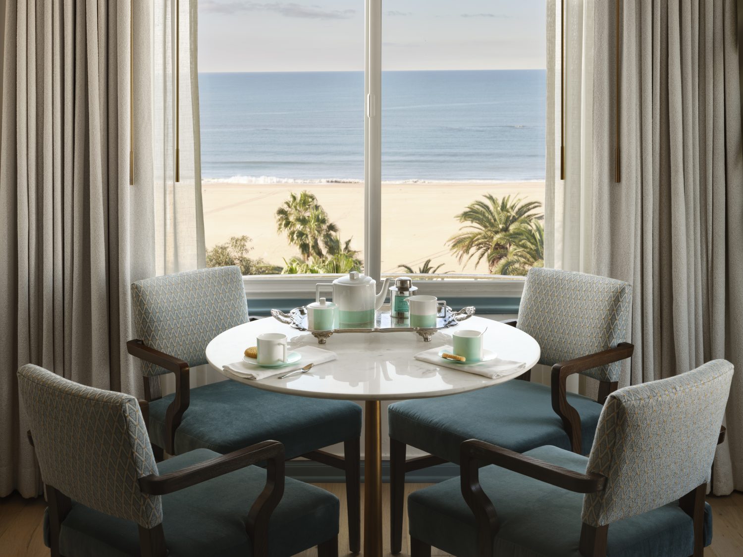 white chairs surrounding table, blue tea set, window with view of beach