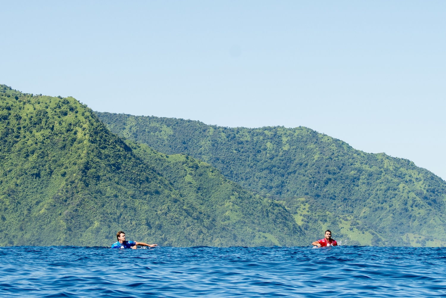 Two surfers swimming in brilliant blue water.