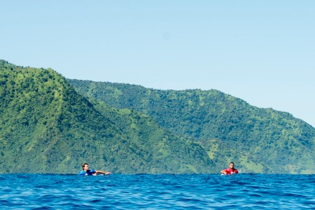 Two surfers swimming in brilliant blue water.