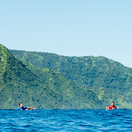 Two surfers swimming in brilliant blue water.