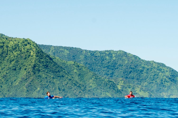 Two surfers swimming in brilliant blue water.