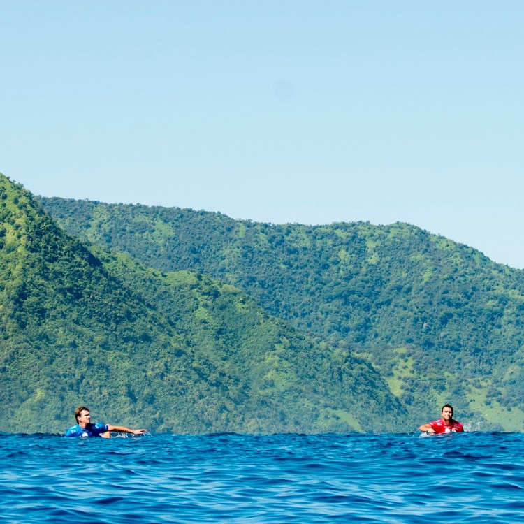 Two surfers swimming in brilliant blue water.