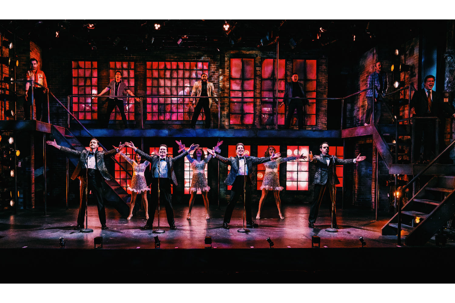 six men upstairs in background, four men in sparkly suits with microphones in foreground, three backup female singers in golden dresses behind them