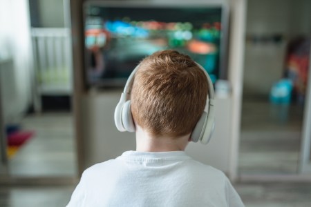 A young boy wearing headphones staring at a TV screen.