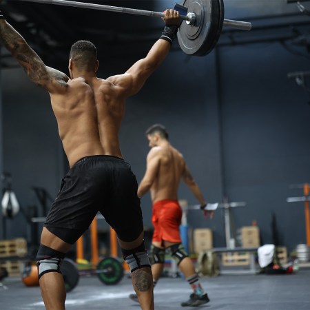 A muscular man lifting a barbell over his head. Here's how strength training can actually give you youthful skin.