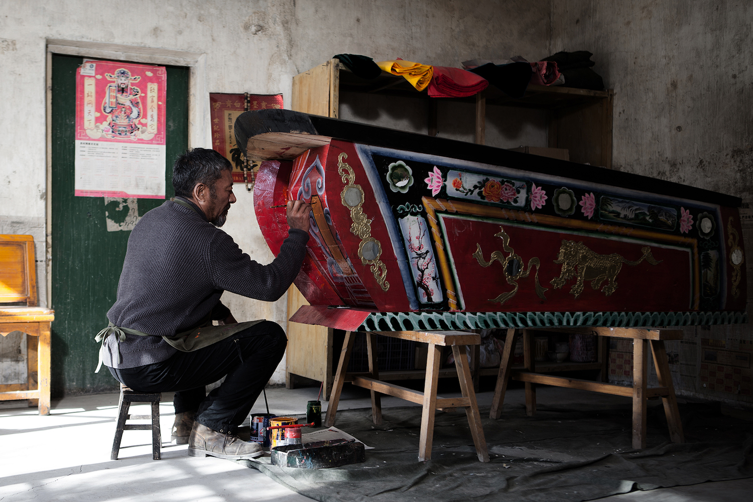 a man sitting on a stool painting a coffin