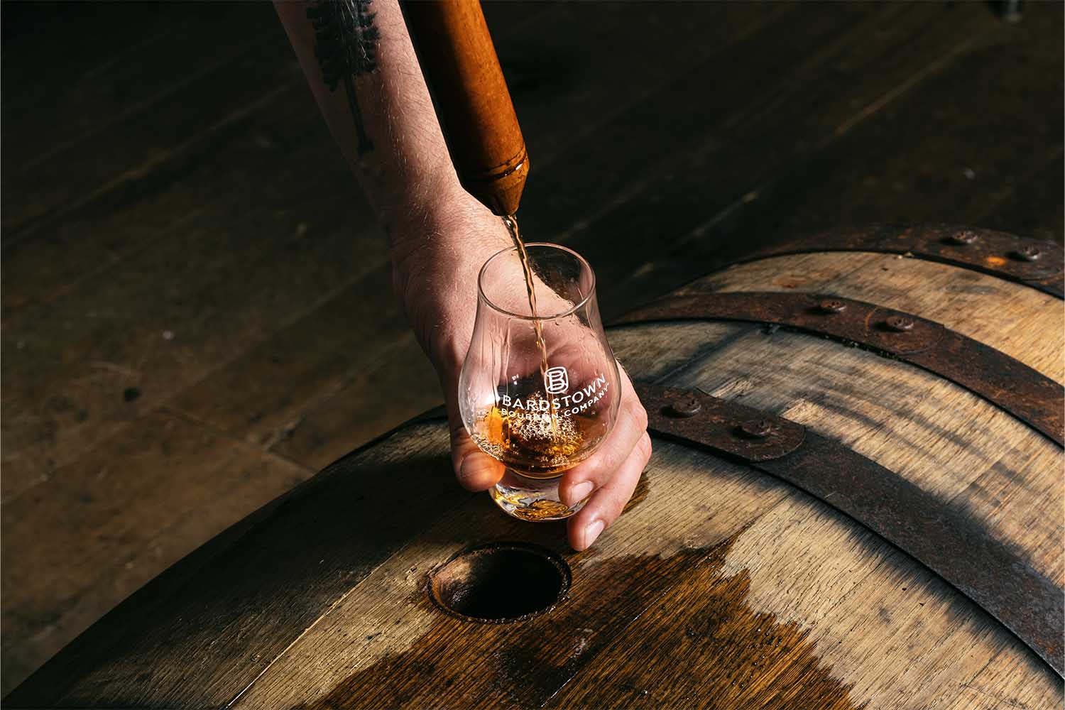 A whiskey thief pouring bourbon from a barrel into a Glencairn at Bardstown Bourbon Company