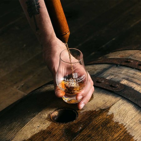 A whiskey thief pouring bourbon from a barrel into a Glencairn at Bardstown Bourbon Company