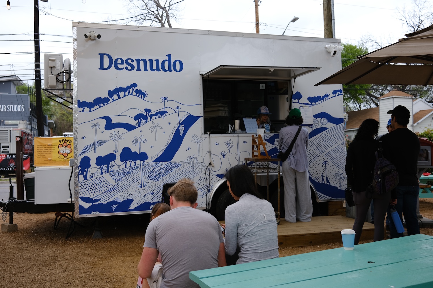white food truck with blue design, people sitting outside, green bench