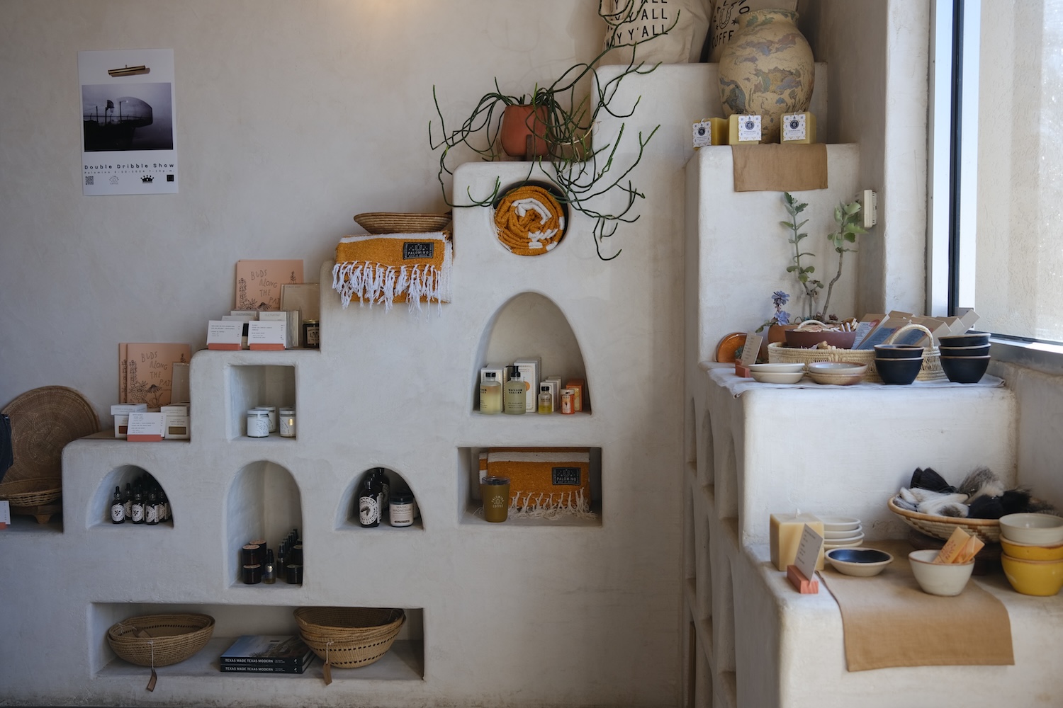 white shelves with towels, oils, bins, ceramics, plant, poster on wall