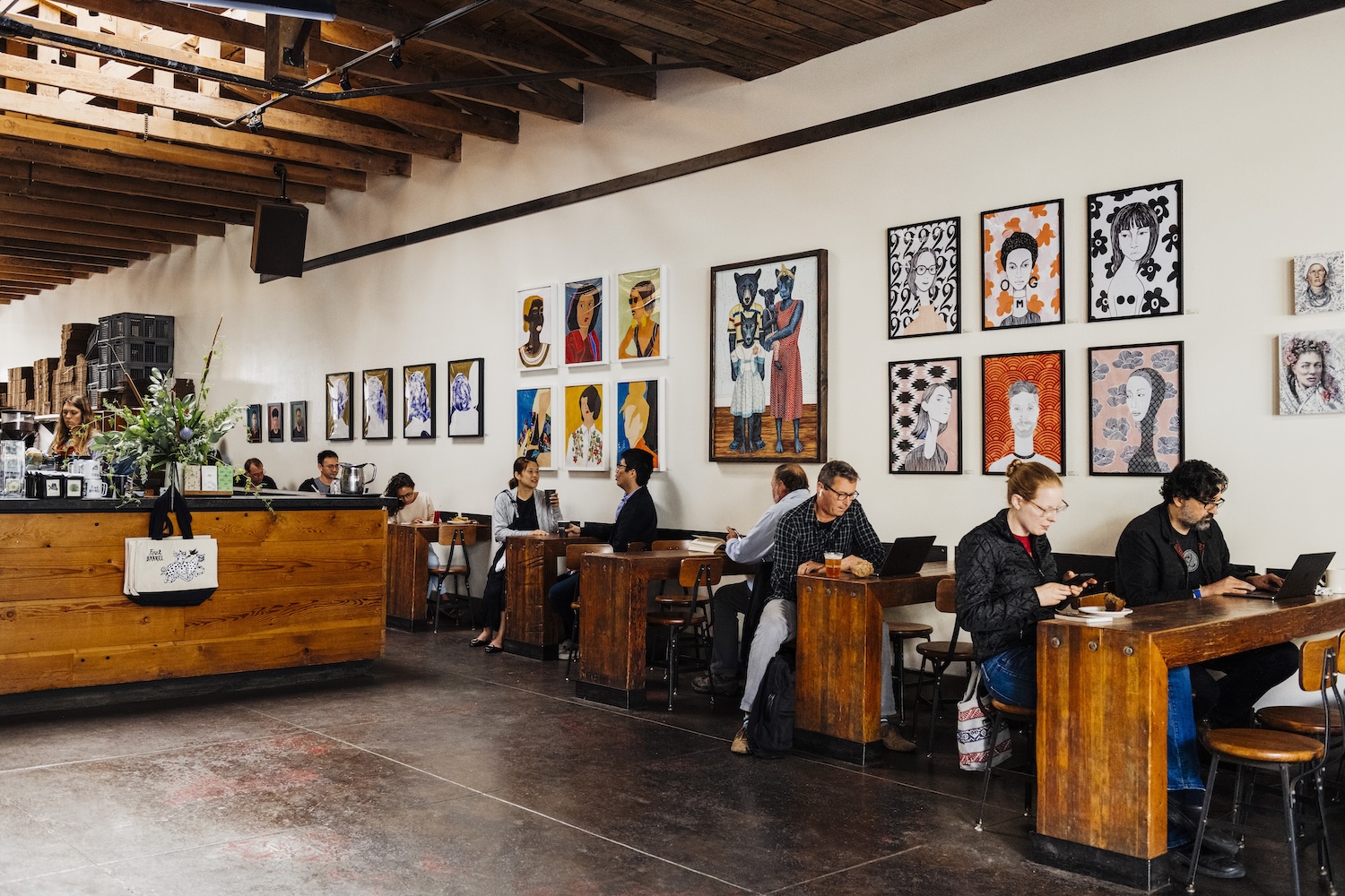 people sitting at wooden tables, paintings on wall, wooden columns on ceiling