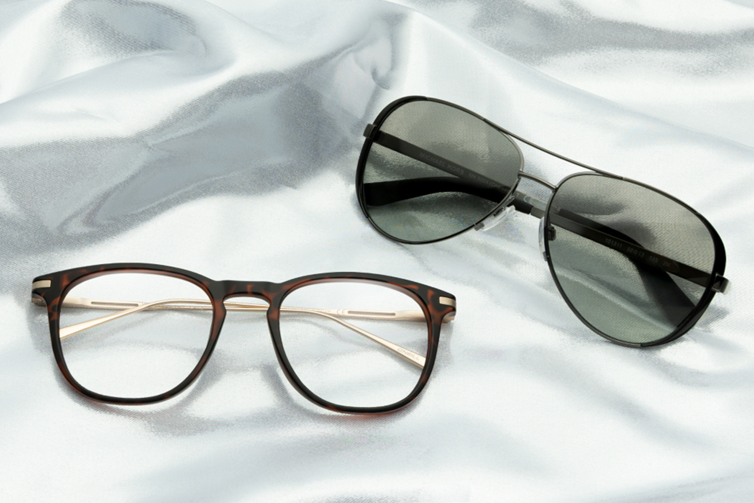 A pair of sunglasses and a pair of eyeglasses sitting on a sheet