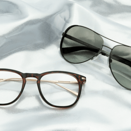 A pair of sunglasses and a pair of eyeglasses sitting on a sheet