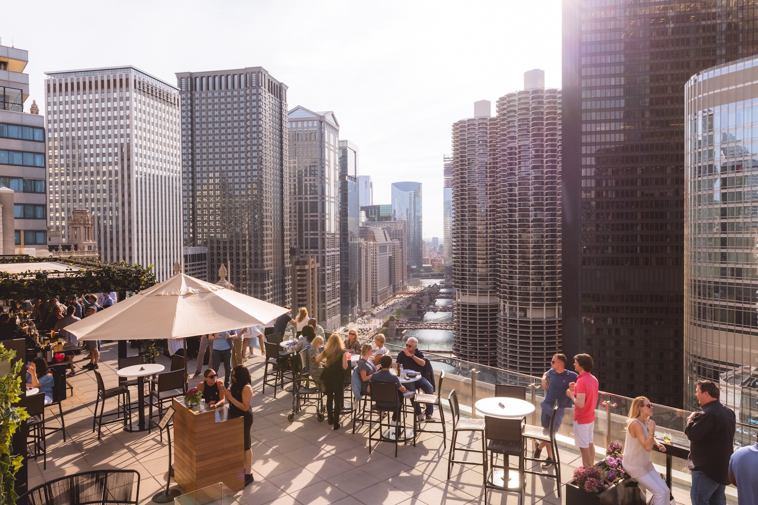 people on rooftop on sunny day, umbrella, chairs and tables, buildings